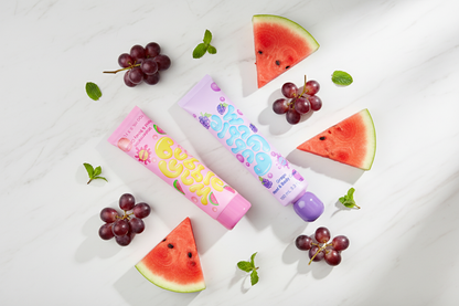 Pink watermelon and purple grape hand cream tubes on marble with fresh fruit on white background