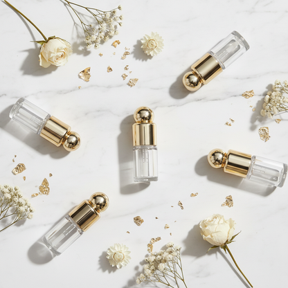 Five gold ball cap lip gloss tubes flatlay on white marble with gold foil and flowers