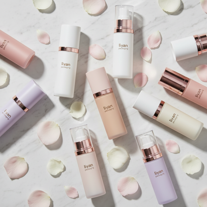 Multiple colored airless pump bottles arranged on marble with rose petals